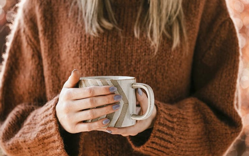lifestyle image of a woman holding a cup of coffee in the fall with painted nails